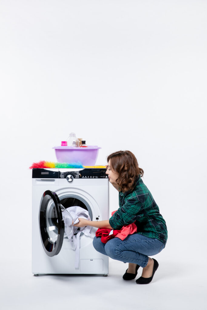 front view young female with washing machine preparing clothes wash white wall